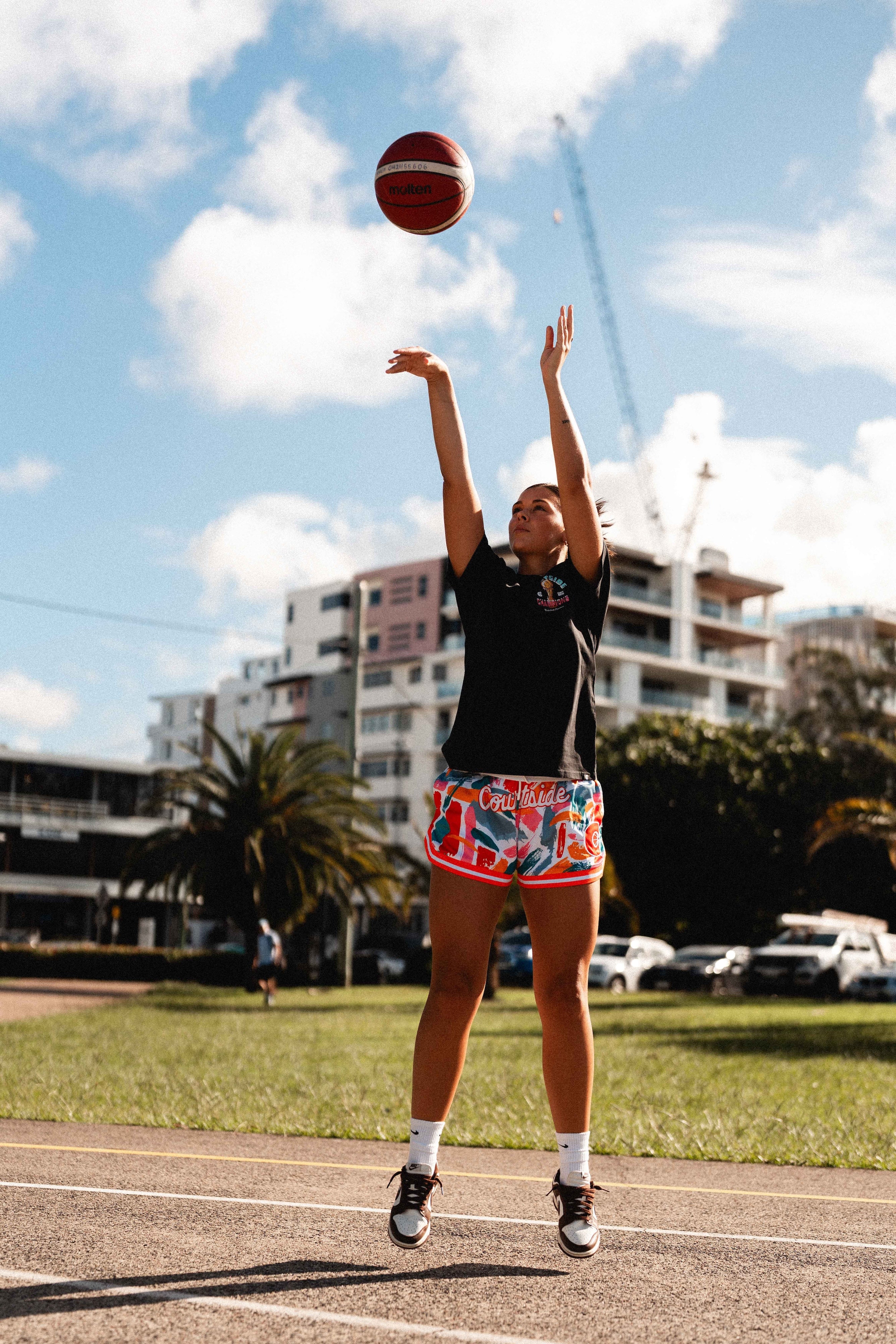 NBL1 player Ash Frampton shooting hoops wearing MVPW orange and colourful basketball shorts and black champs tee at Cotton Tree outdoor court in Sunshine Coast