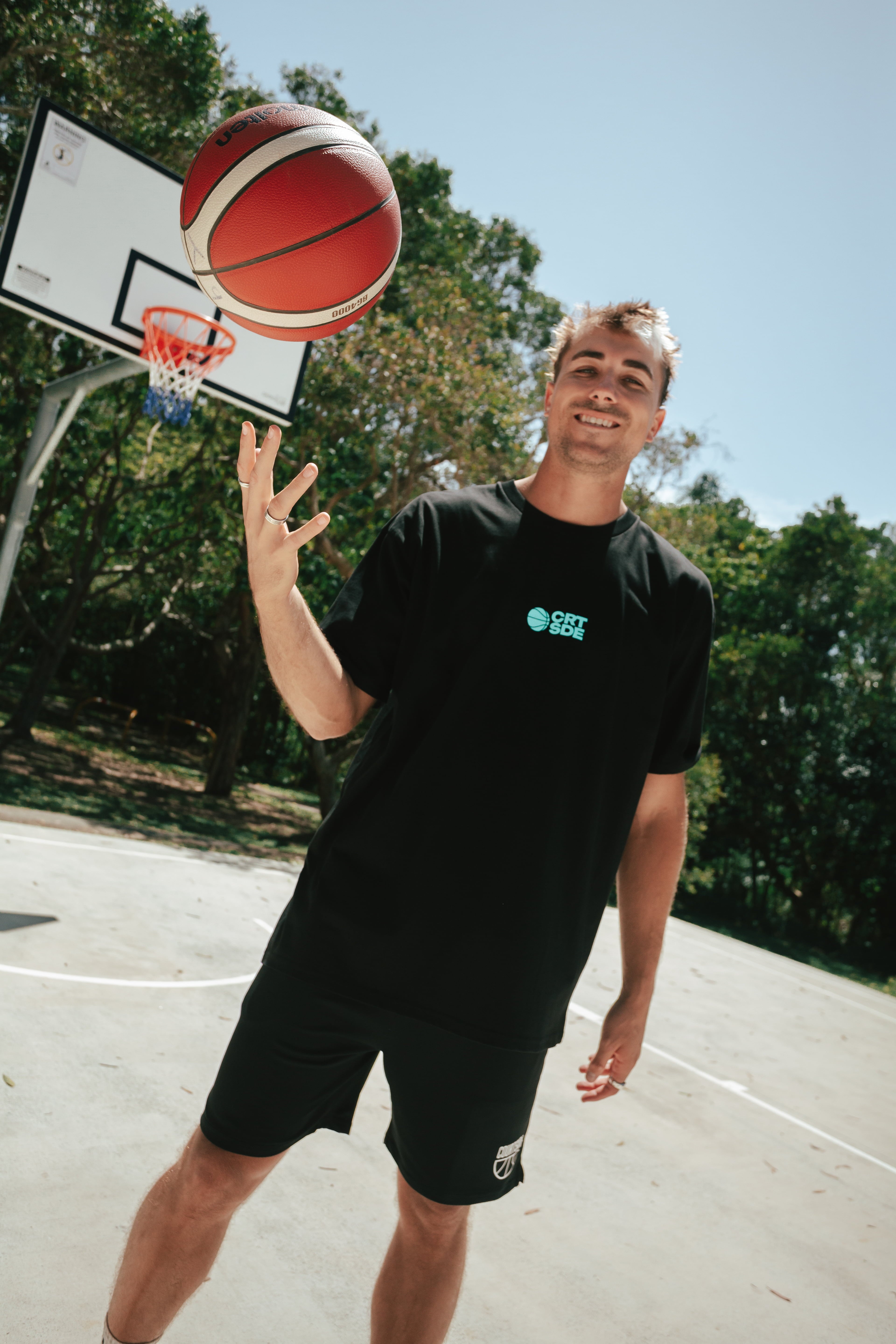 Black basketball netted shorts, narrow fit, long legged, traditional short with white courtside logo on bottom left leg front shown on smiling basketball player Nelson Kahler