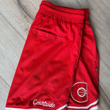 Red basketball shorts with a logo and 'Courtside' text on a wooden floor.