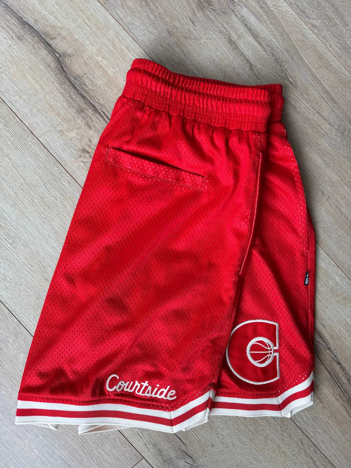 Red basketball shorts with a logo and 'Courtside' text on a wooden floor.
