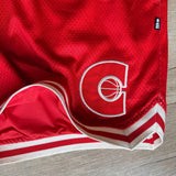 Red mens basketball shorts with a logo on a wooden surface