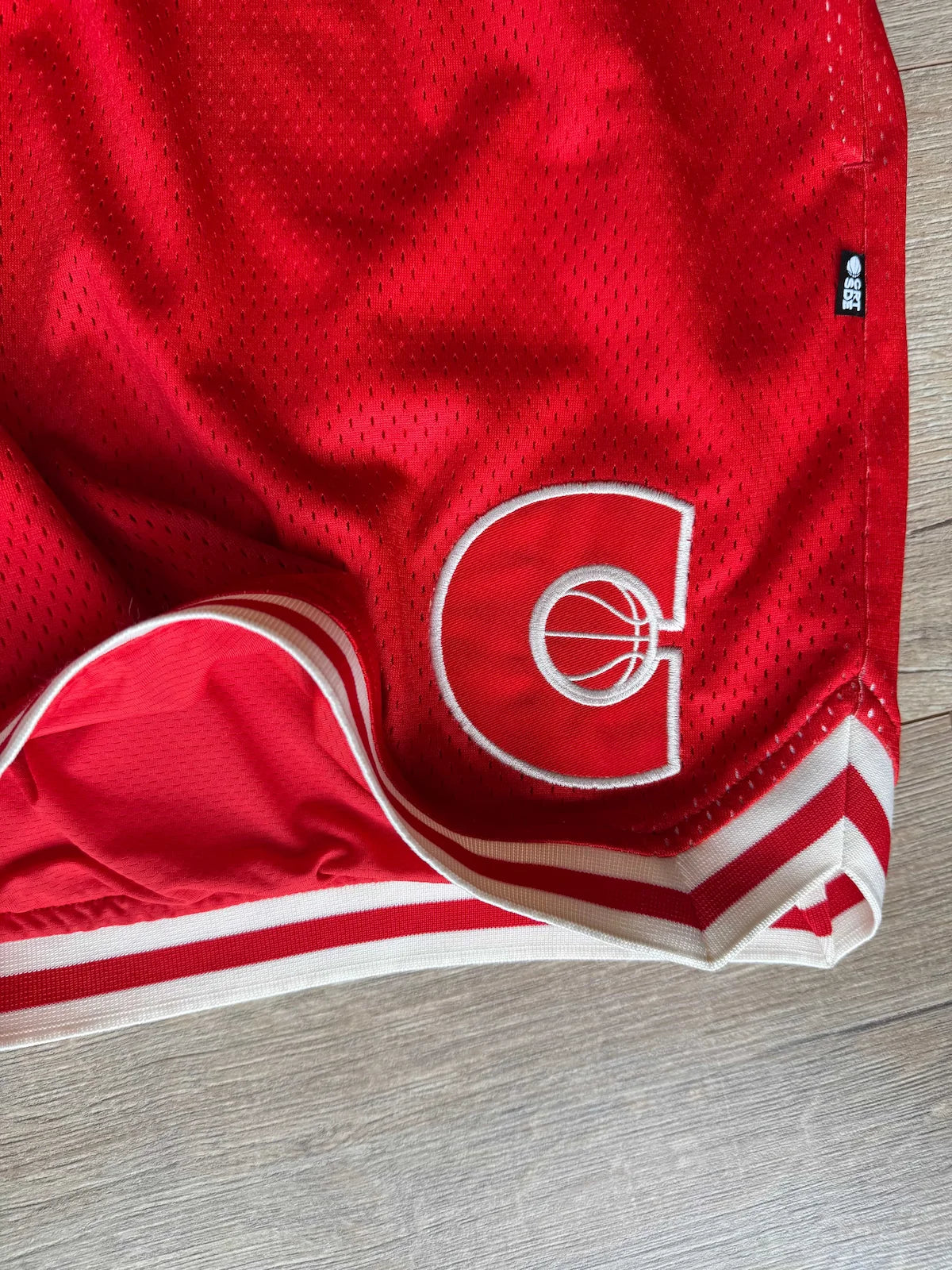 Red mens basketball shorts with a logo on a wooden surface