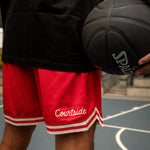 Person wearing red 'Courtside' shorts holding a black basketball on a court.