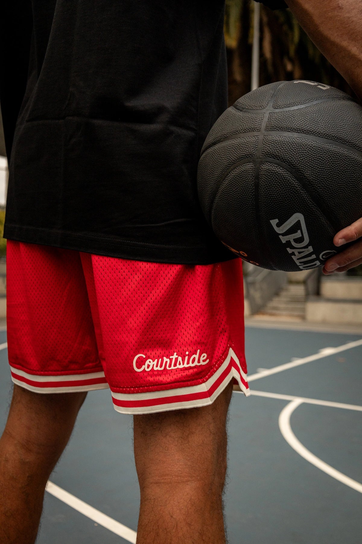 Person wearing red 'Courtside' shorts holding a black basketball on a court.