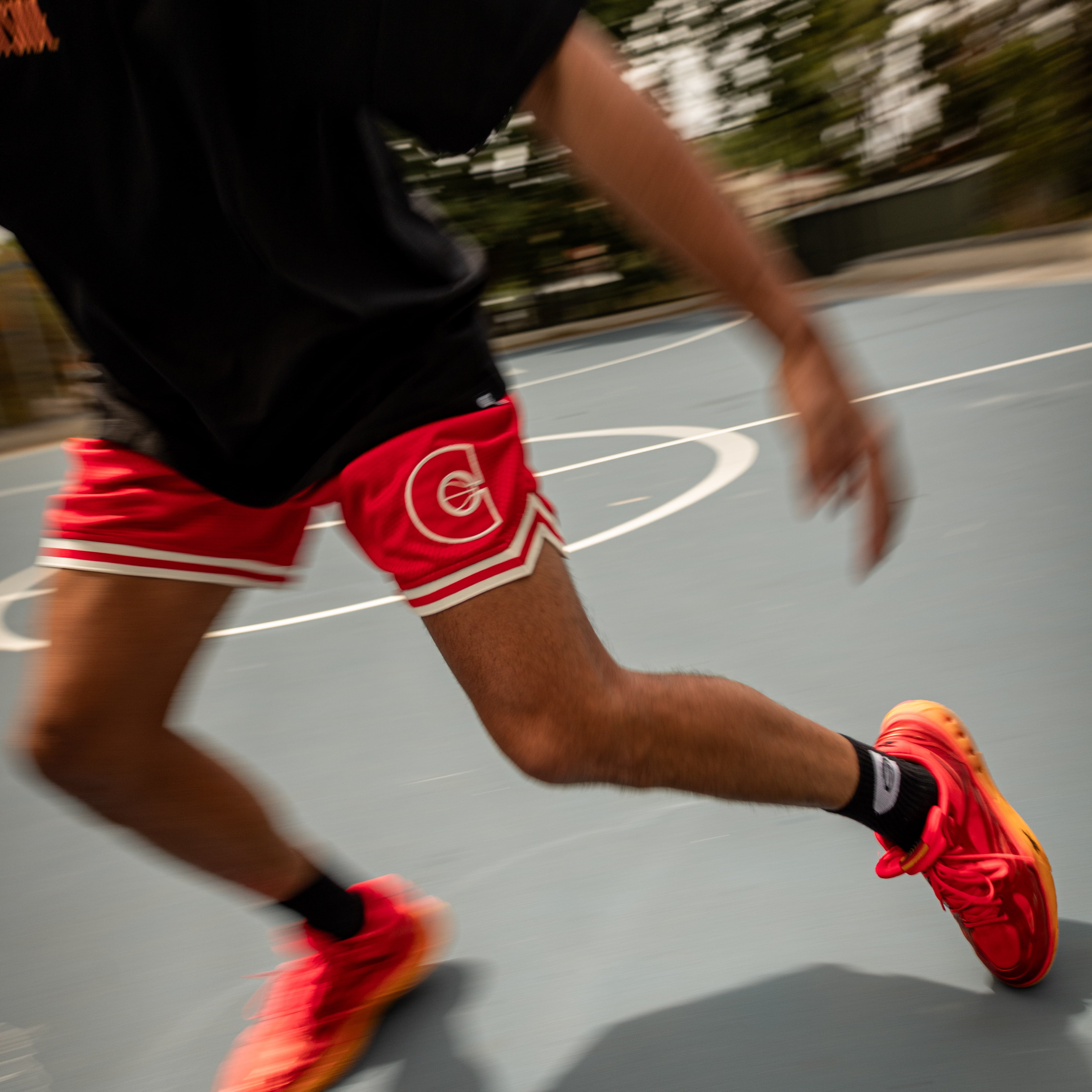 Person running on a basketball court wearing red shoes and shorts.