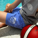 bright blue shorts shown worn by young person sitting beside the pool with basketball under arm