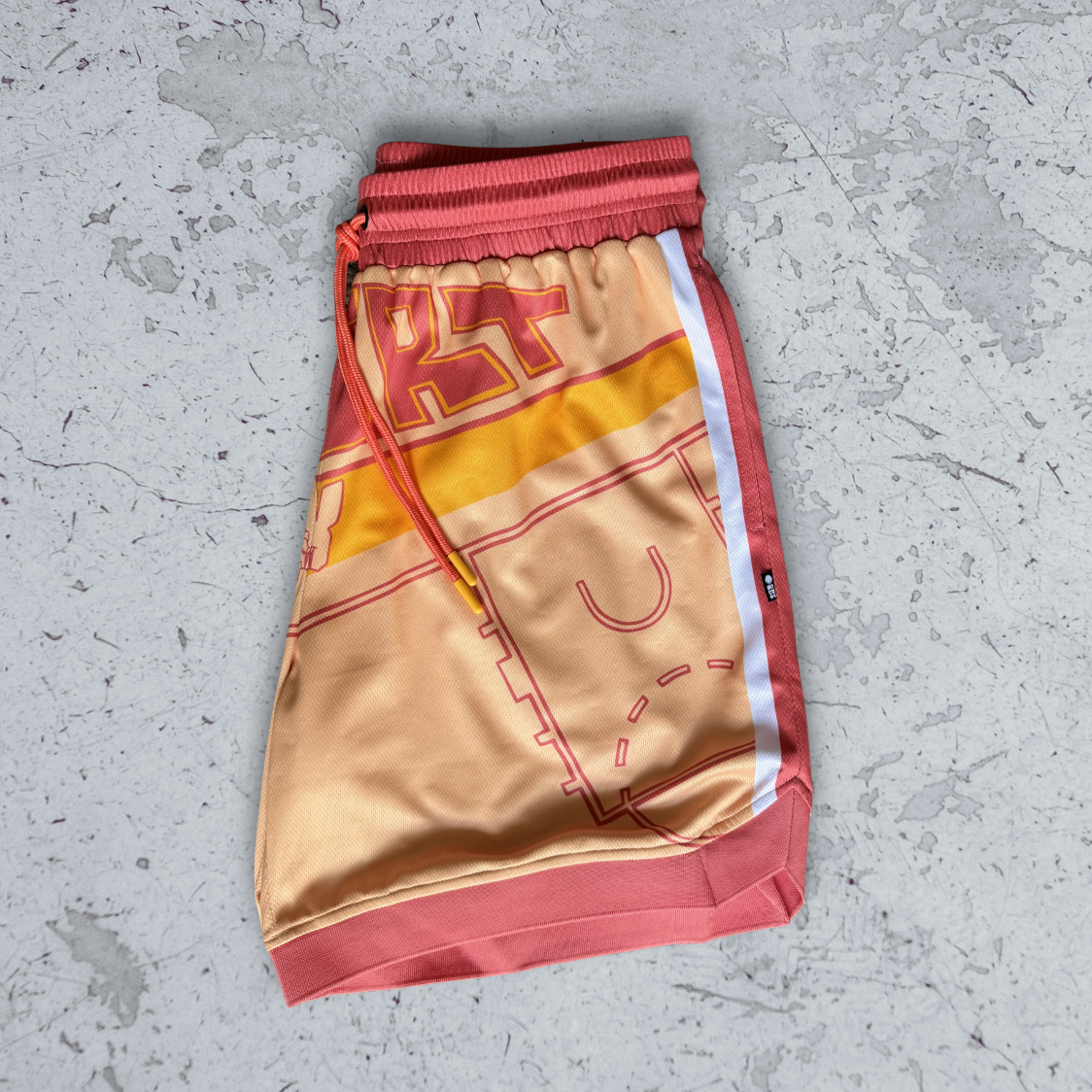 Graphic art on a pair of Courtside basketball shorts in yellow, beige and faded red, shown on a concrete floor