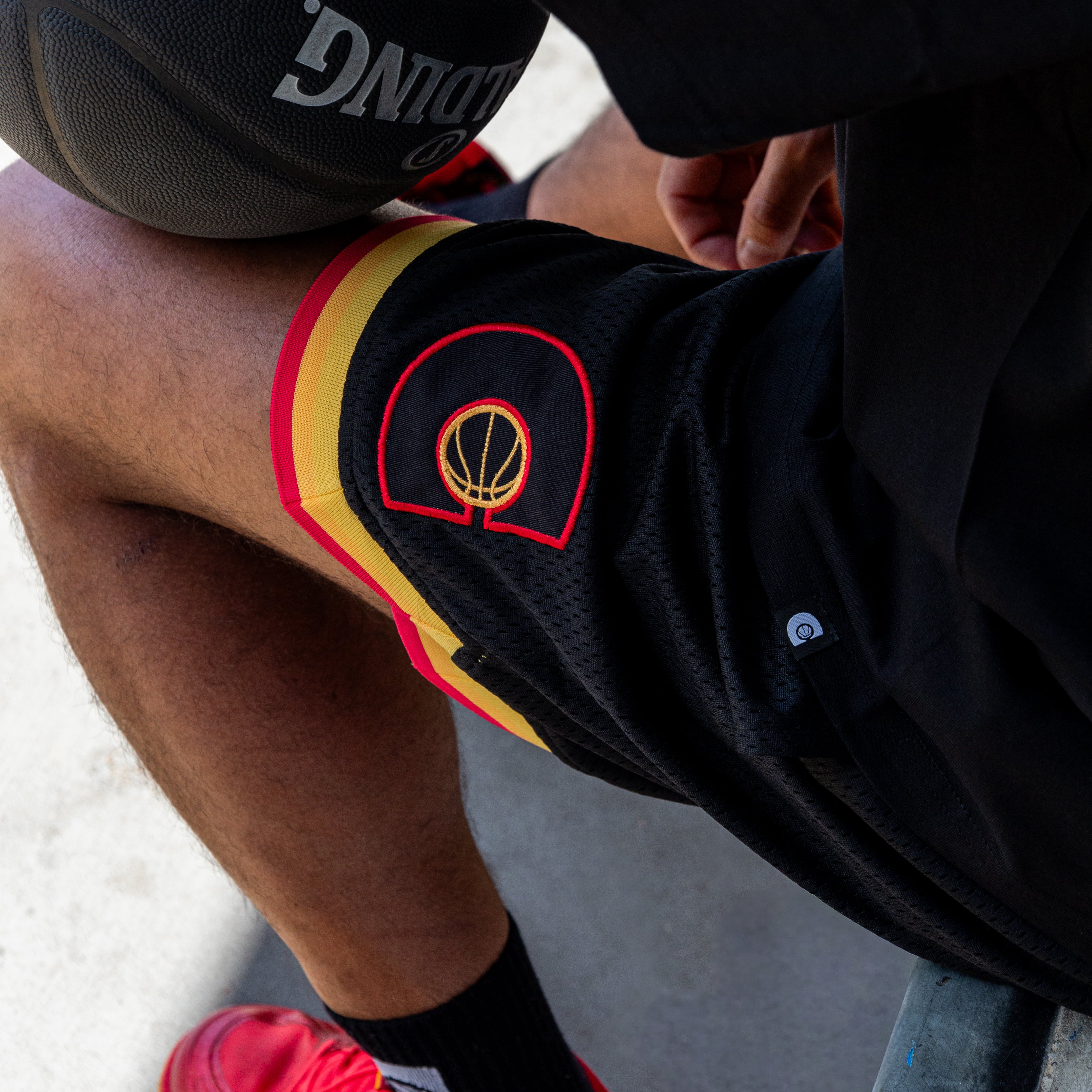 Person wearing black shorts with a red and yellow logo, red shoes, and black courtside socks.