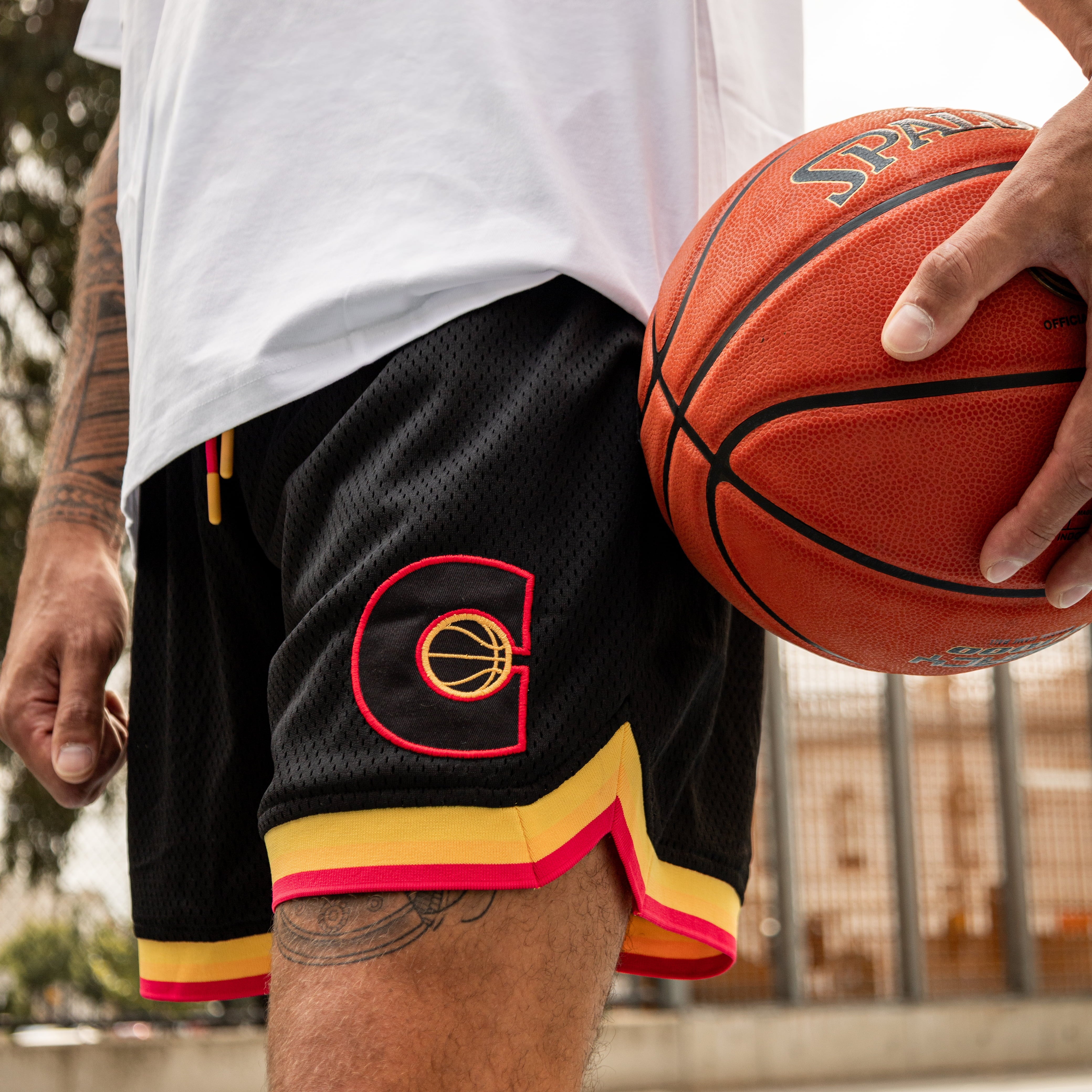 Person holding a basketball wearing black shorts with a C logo, outdoors.