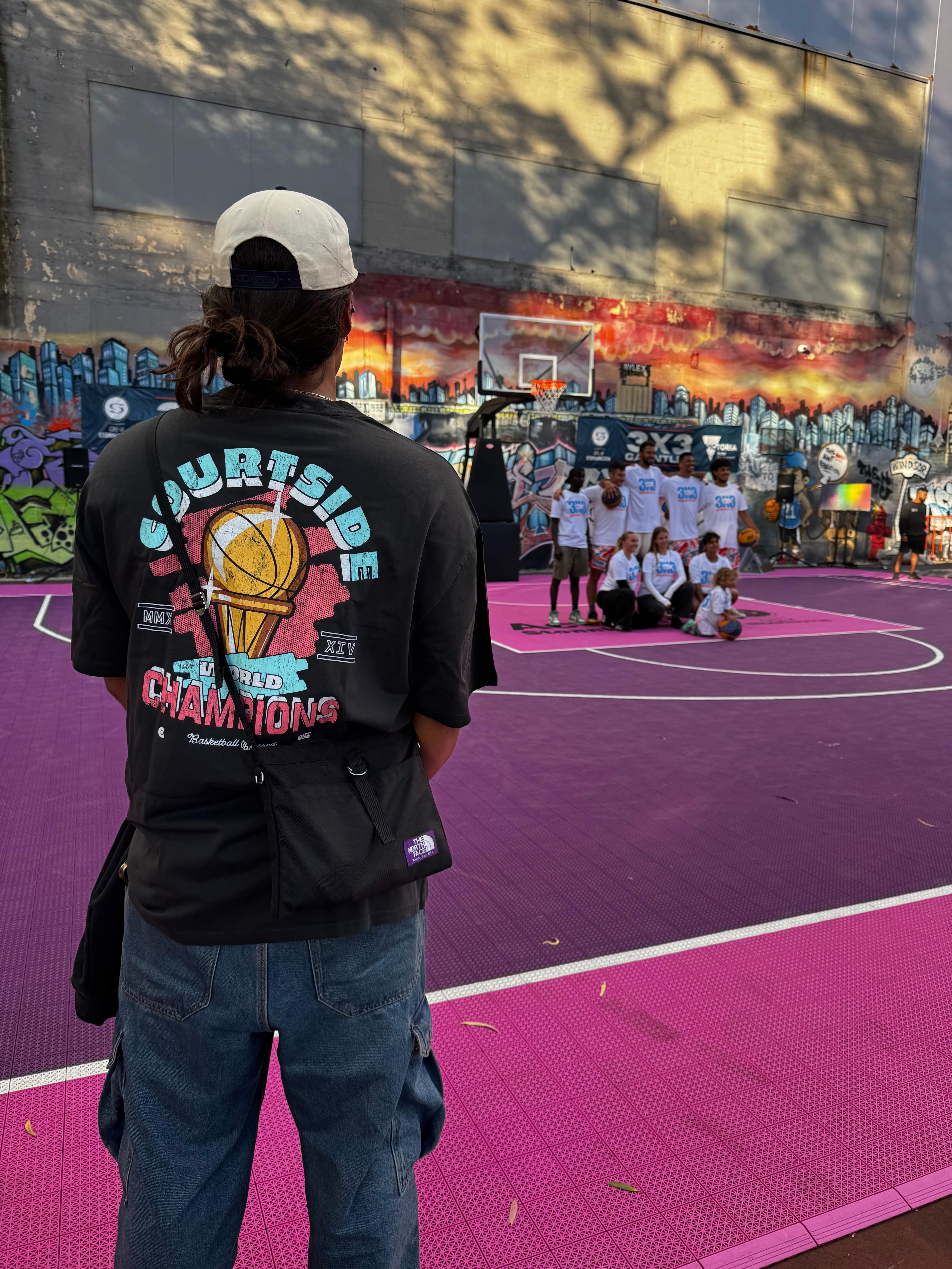 showing back of the champs tee worn on melbourne hooper and freestyle rapper whilst watching community basketball competition