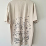 Bone t-shirt with black handdrawn graphic design on back, placed on a wooden hanger against a white wall