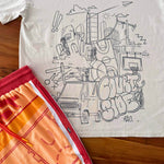 Bone t-shirt with black cityscape graphic and orange basketball shorts on a wooden surface