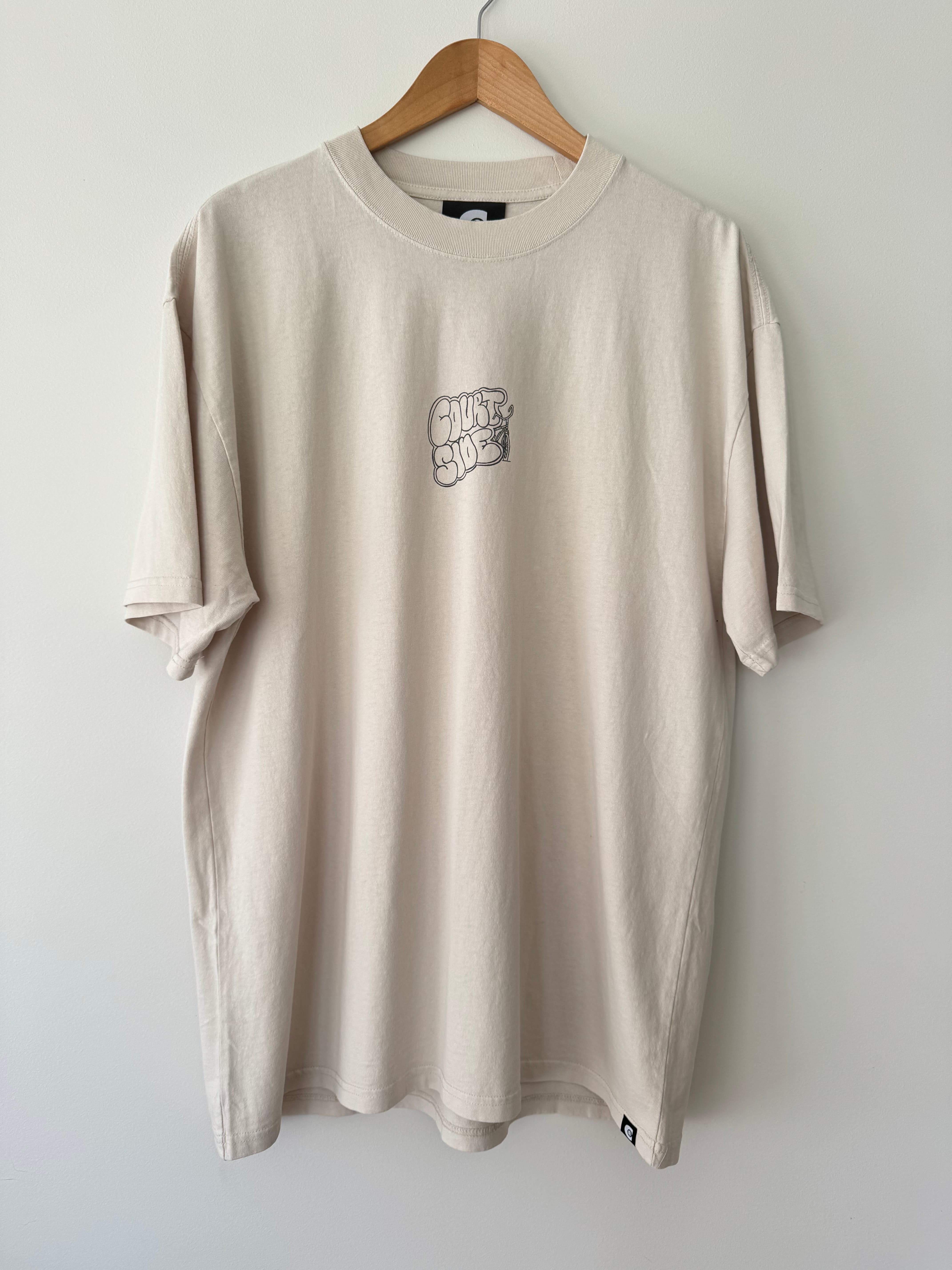 Bone beige t-shirt with a Courtside logo on front chest hanging on a wooden hanger against a white wall