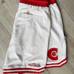 Cream basketball shorts with red details laid on a timber floor