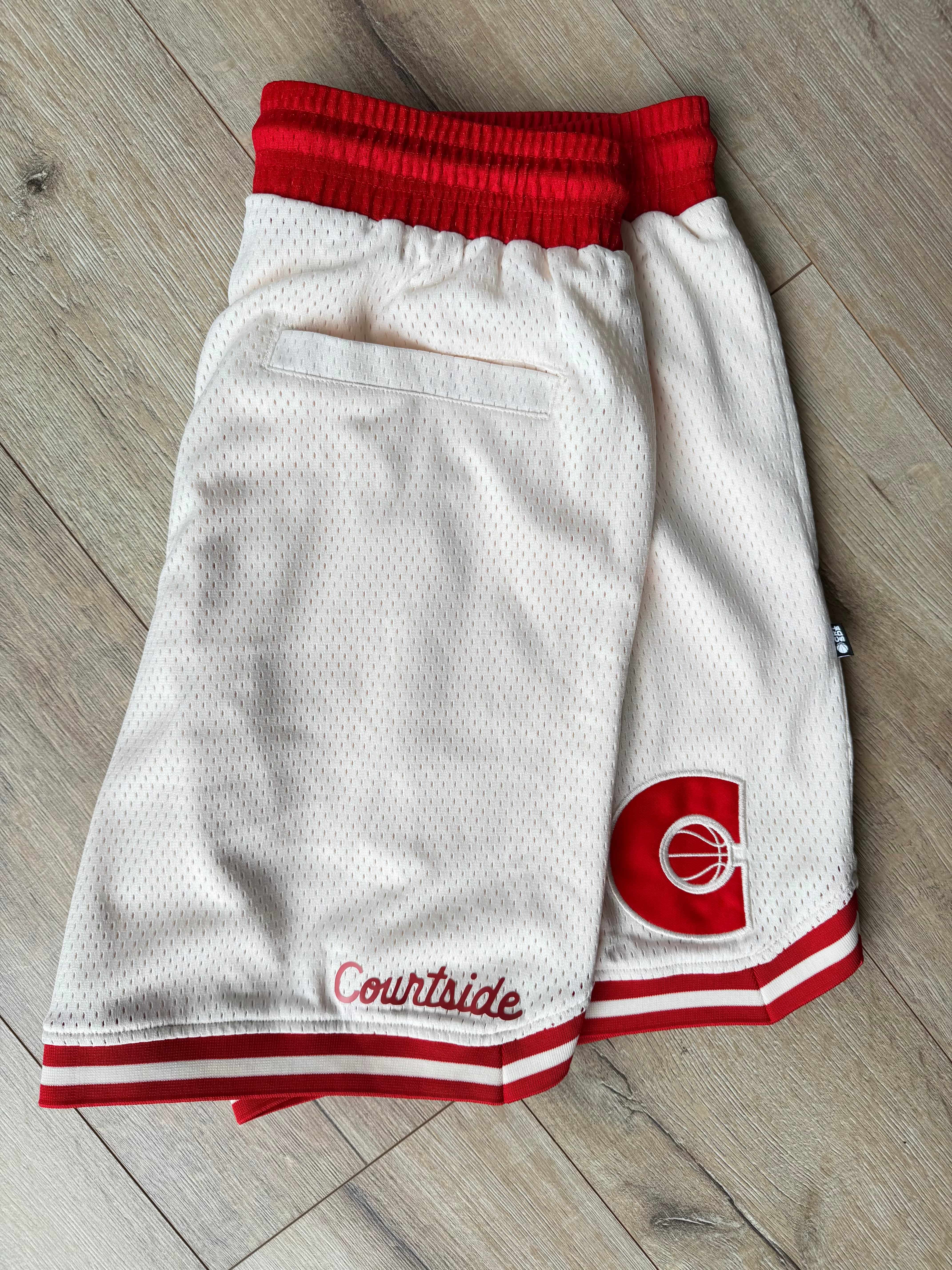 Cream basketball shorts with red details laid on a timber floor