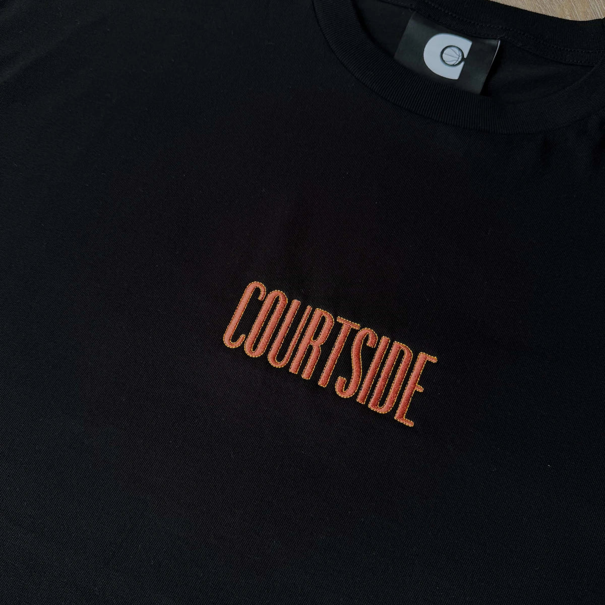 Black t-shirt with 'COURTSIDE' text in orange on a wooden surface