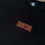 Black t-shirt with 'COURTSIDE' text in orange on a wooden surface