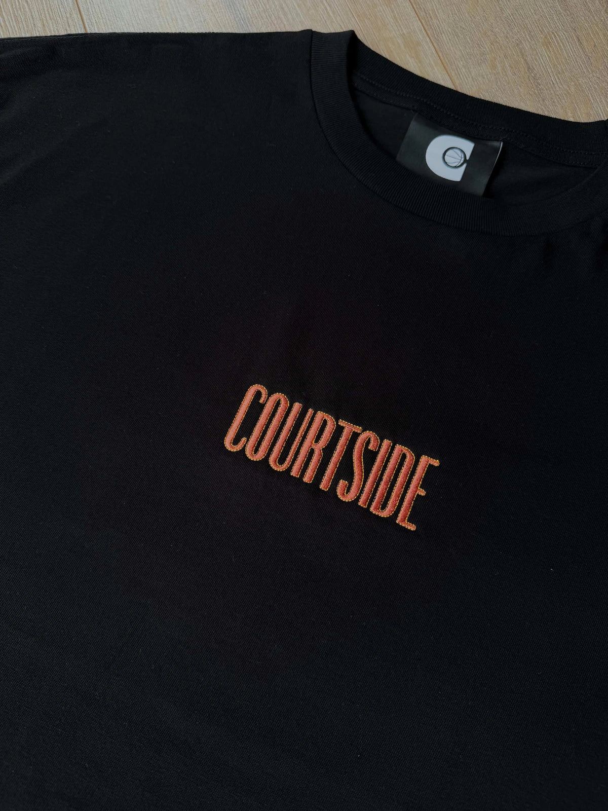 Black t-shirt with 'COURTSIDE' text in orange on a wooden surface