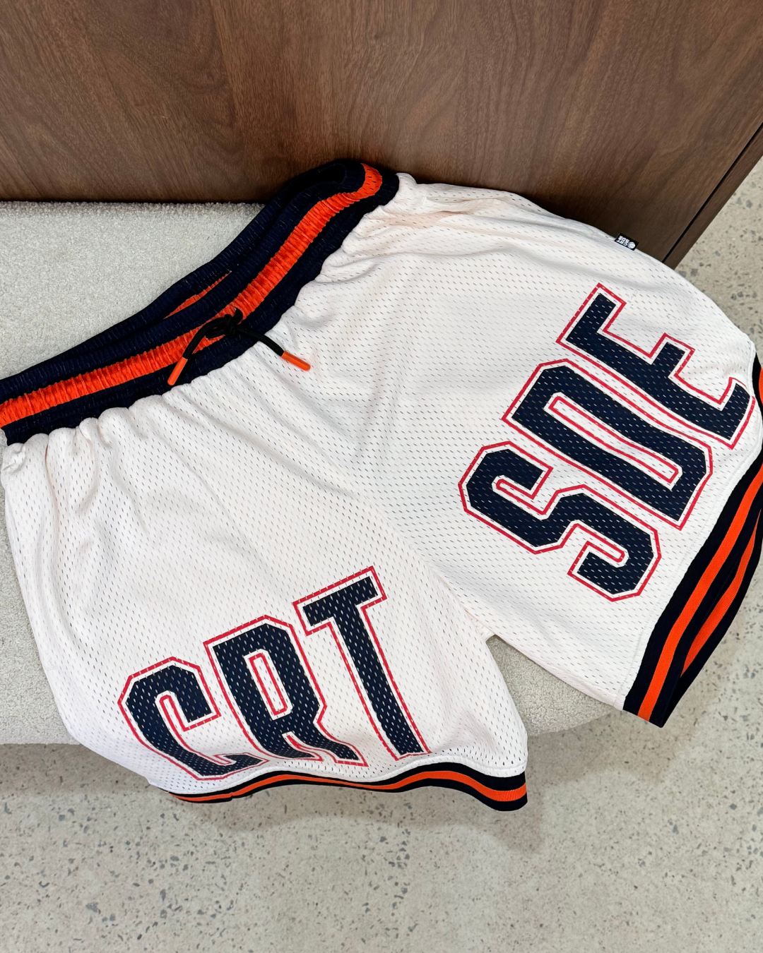 Cream basketball shorts with orange and black accents on a concrete floor.