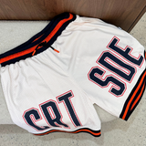 Cream basketball shorts with orange and black accents on a concrete floor.