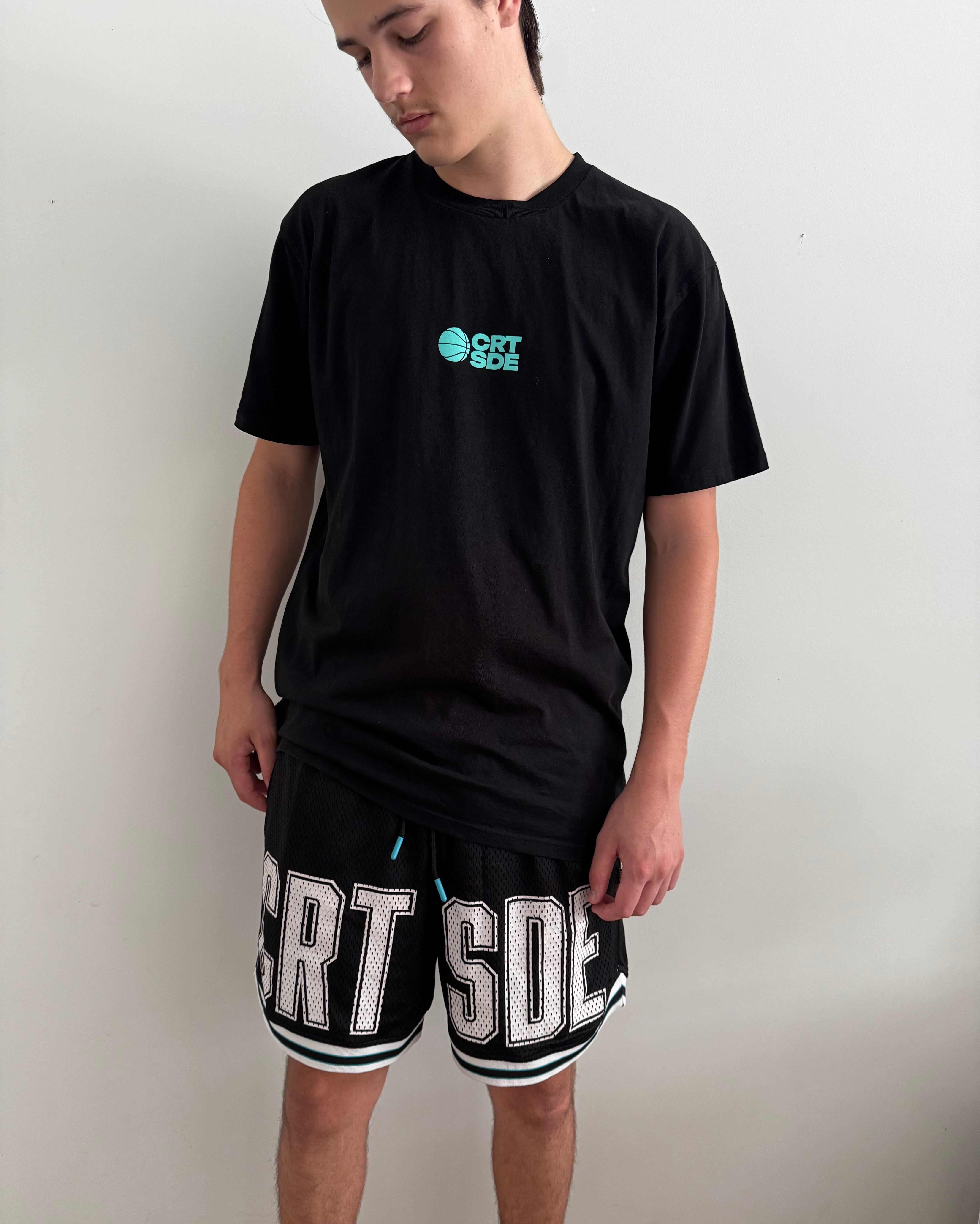Black basketball shorts on tall male with white large letters across front CRT SDE short for Courtside with Teal detailing.