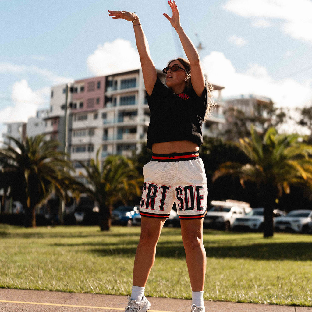 Courtside DPOY basketball shorts in cream with orange & black highlights, shown on NBL1 player Nicola Watkins shooting a basket