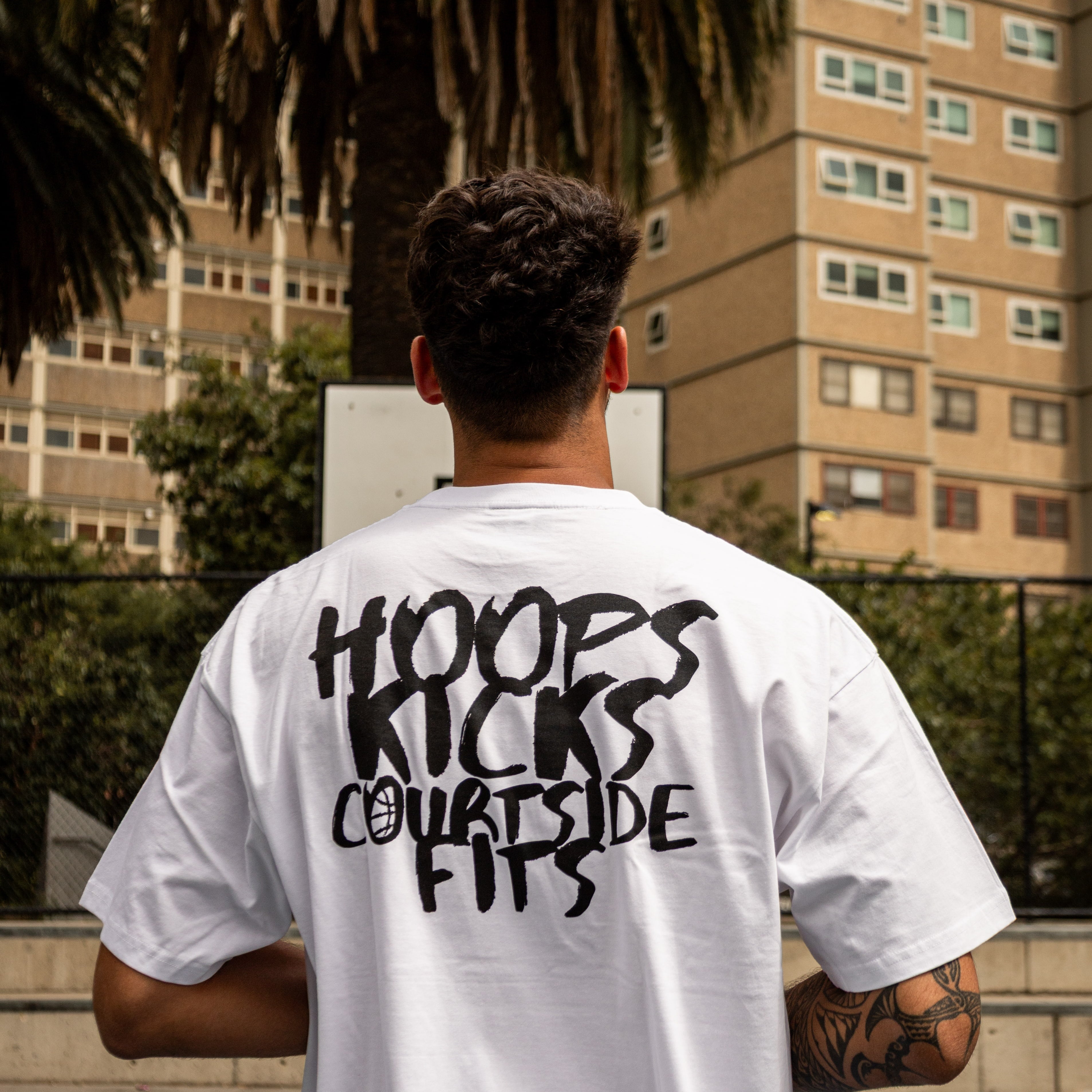 Person wearing a white t-shirt with text on the back, standing on a basketball court.