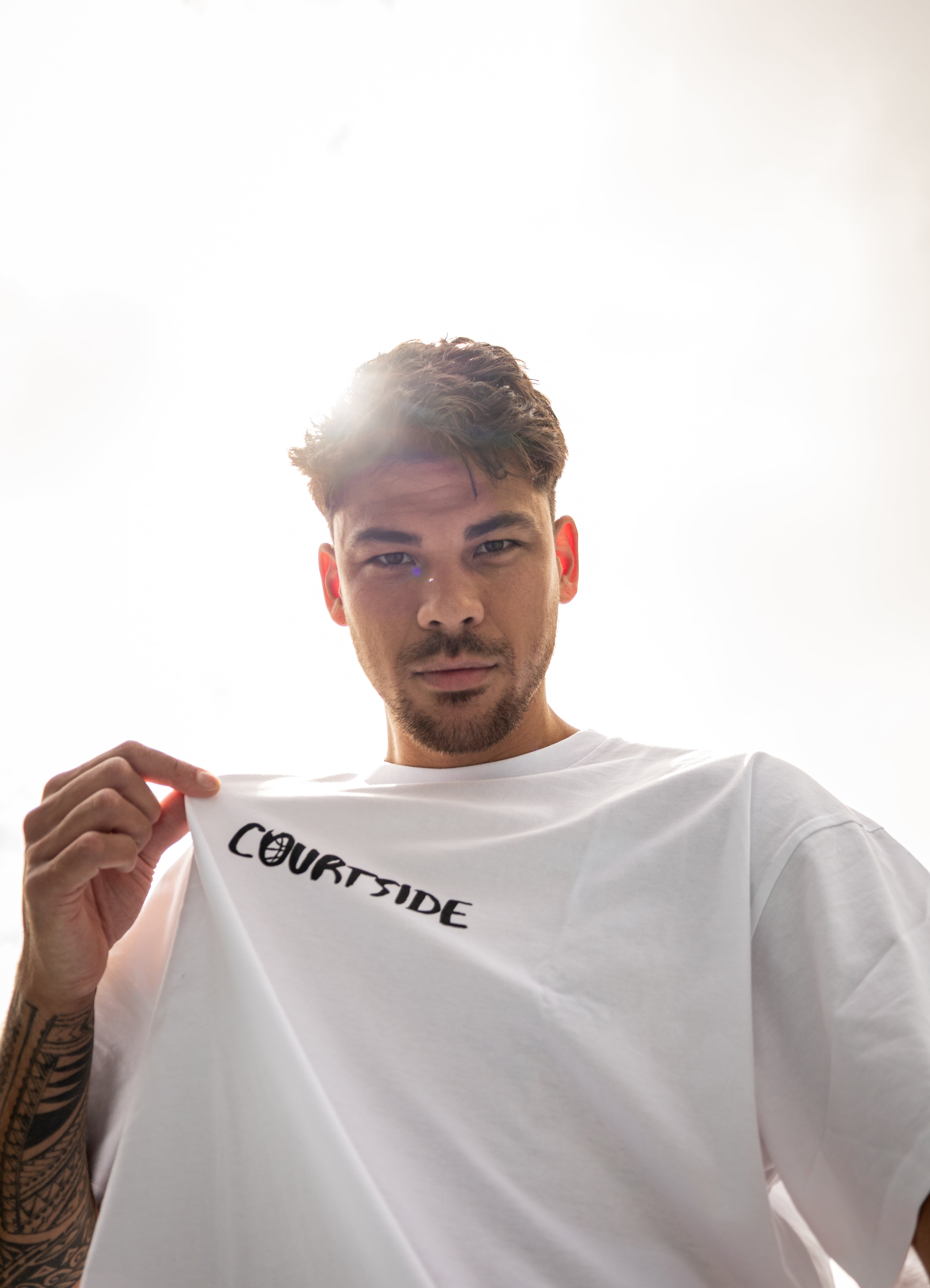 Man holding a white t-shirt with 'COURTSIDE' text against a bright background