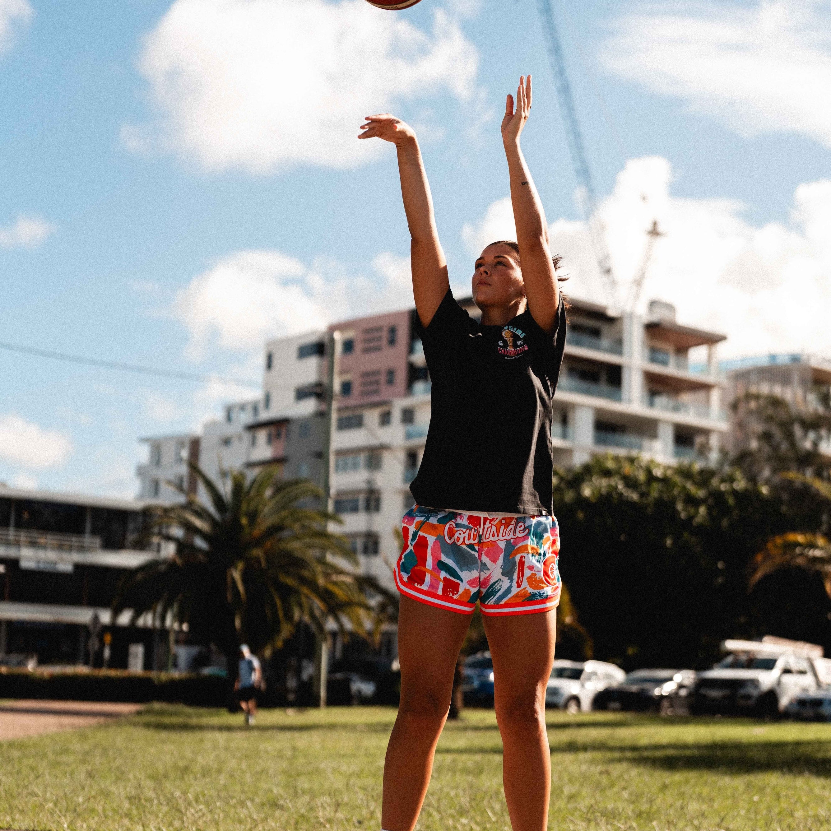 NBL1 player Ash Frampton shooting hoops wearing MVPW orange and colourful basketball shorts and black champs tee at Cotton Tree outdoor court in Sunshine Coast