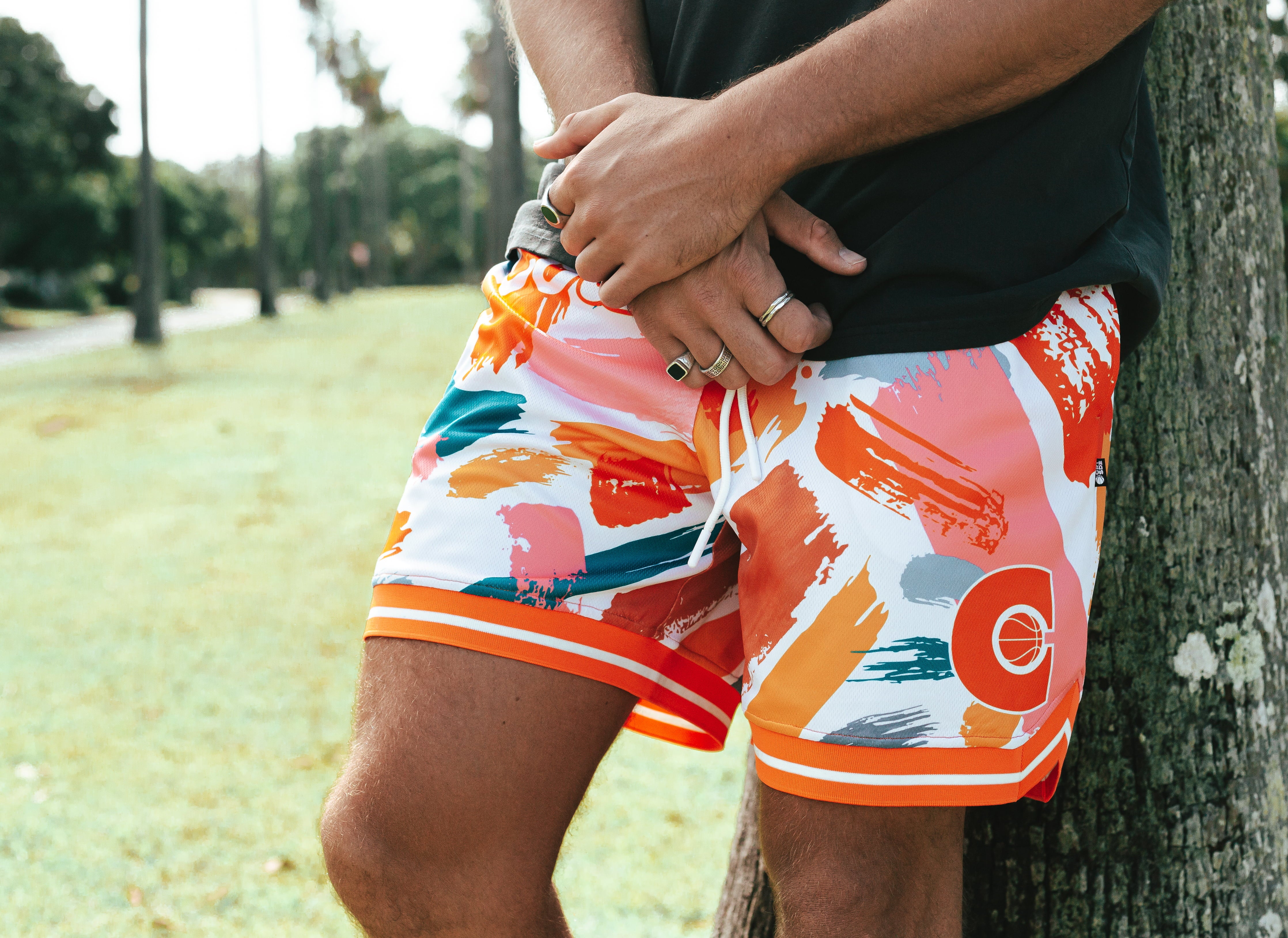 Nelson Kahler NBL player wear orange and white coloured patterned shorts leaning up against palm tree