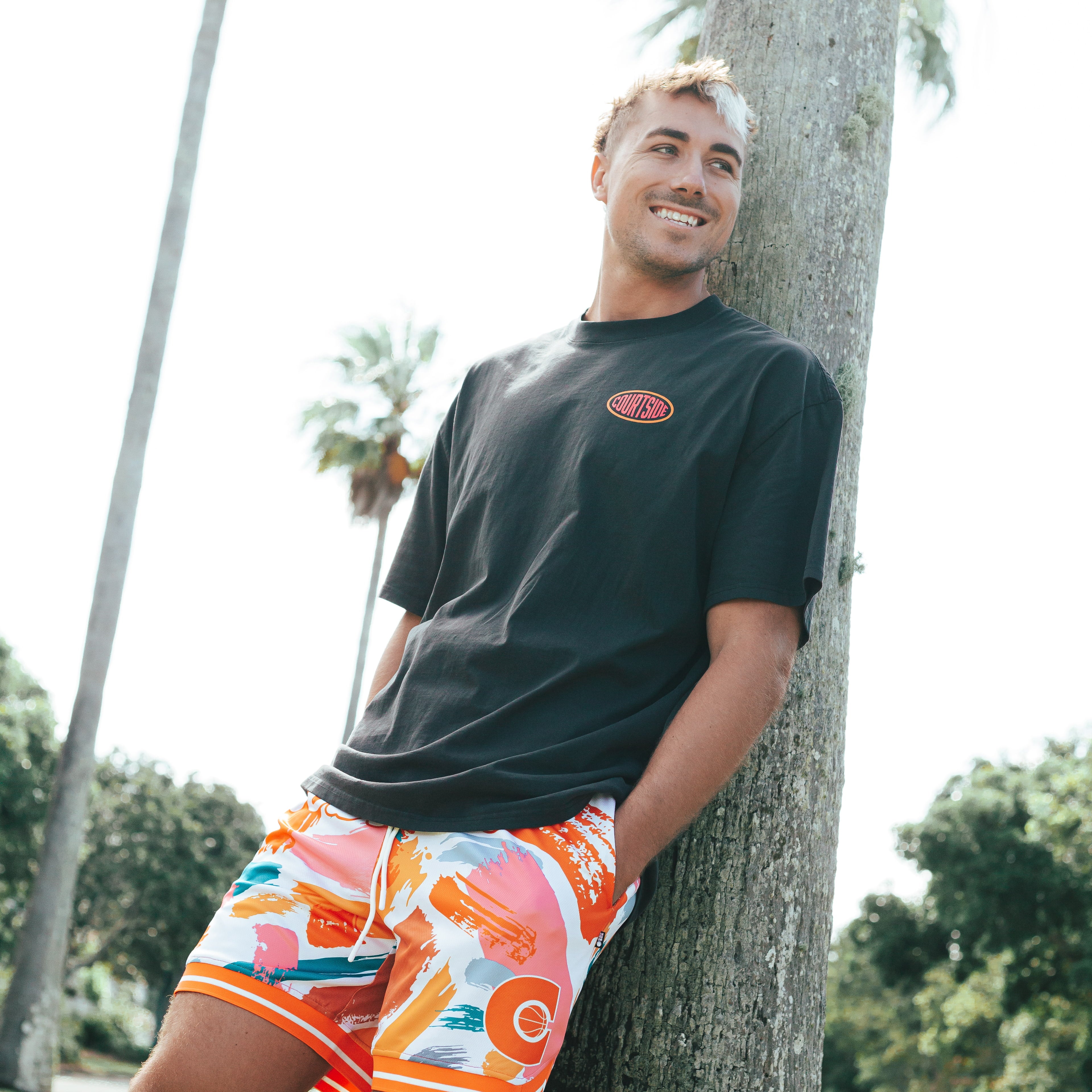 Courtside MVP basketball short shown on Nelson Kahler NBL player with a black streetball tee leaning against a palm tree