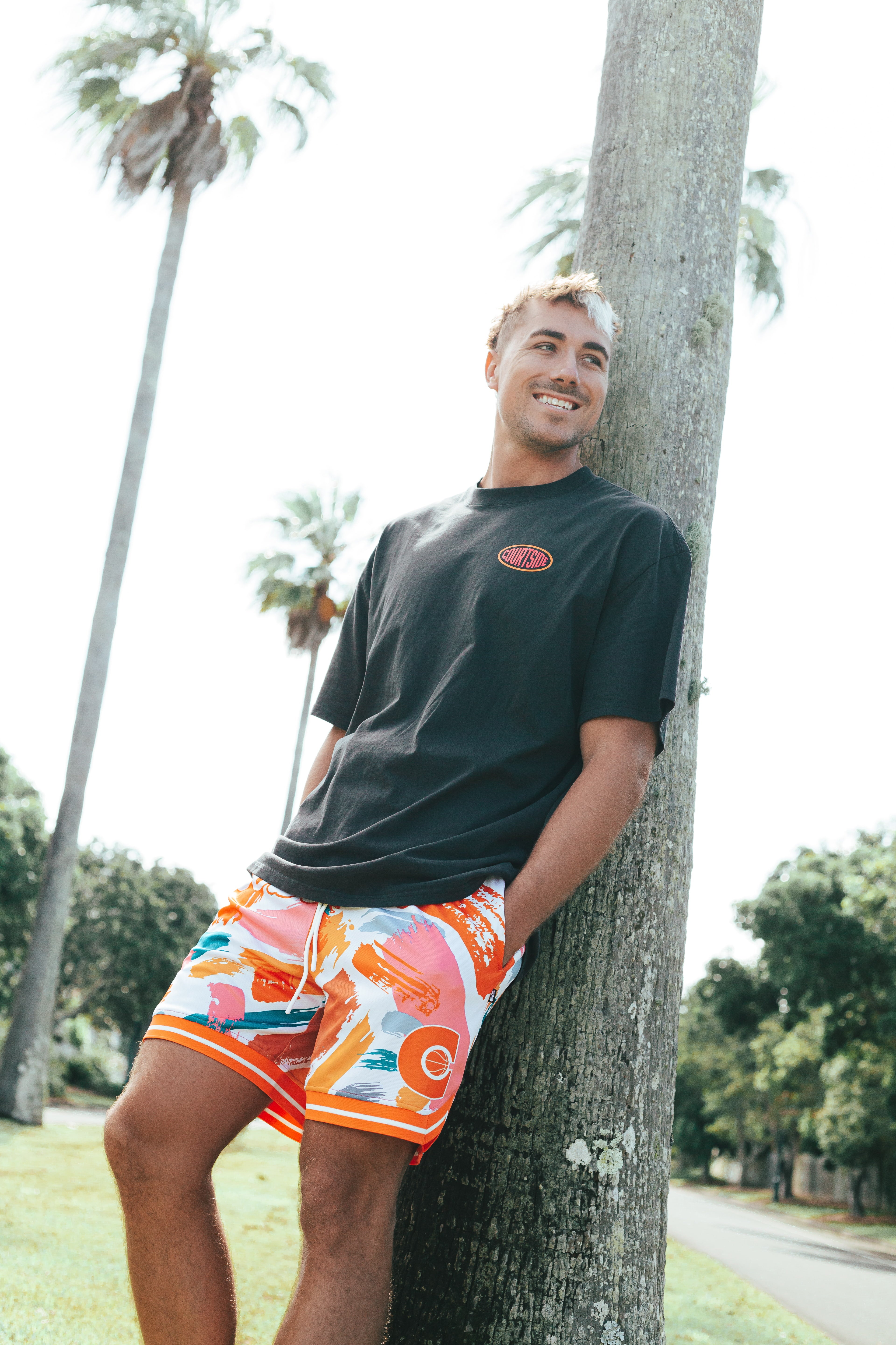Courtside MVP basketball short shown on Nelson Kahler NBL player with a black streetball tee leaning against a palm tree