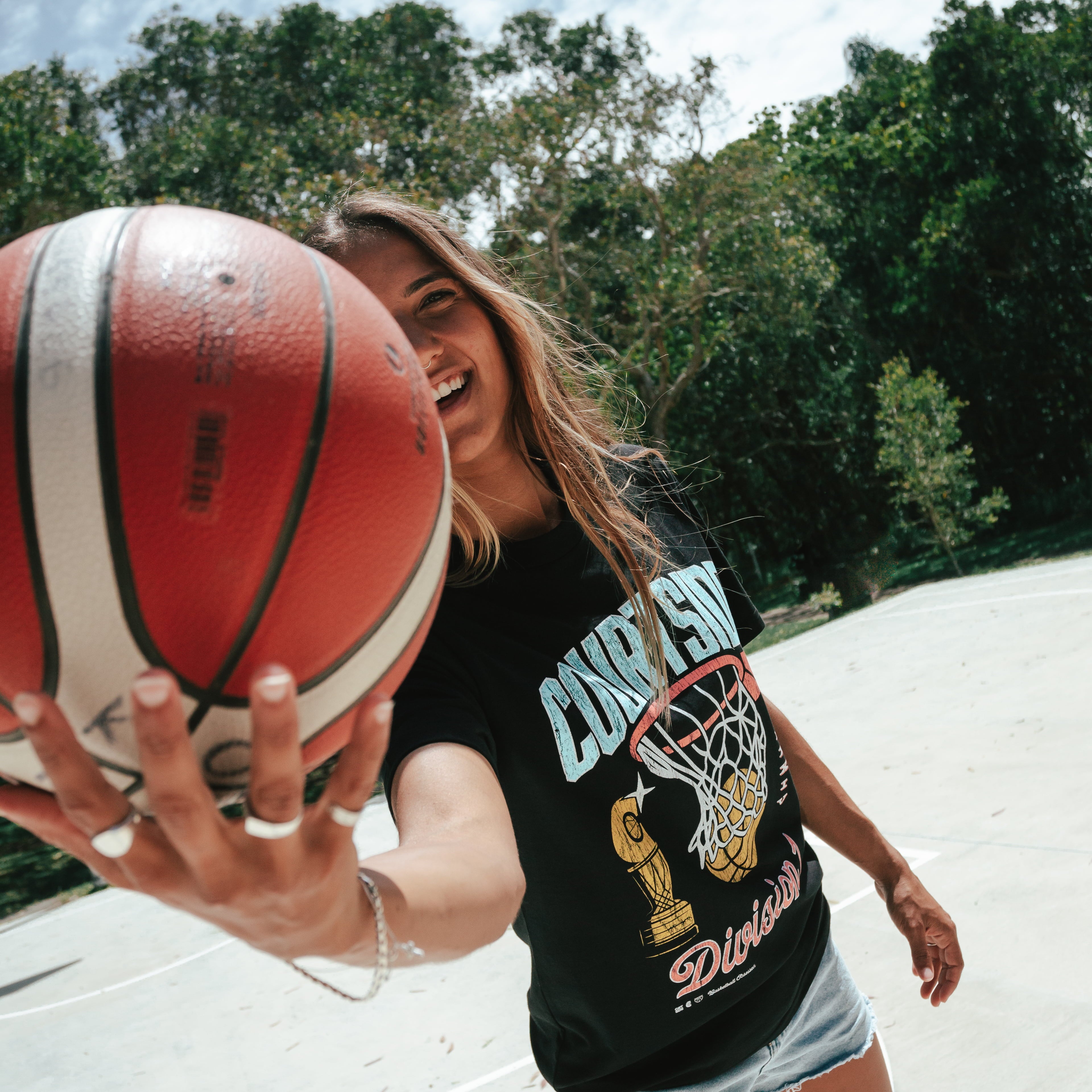 A person wearing a black t-shirt with vintage basketball graphics holding a red and white basketball.