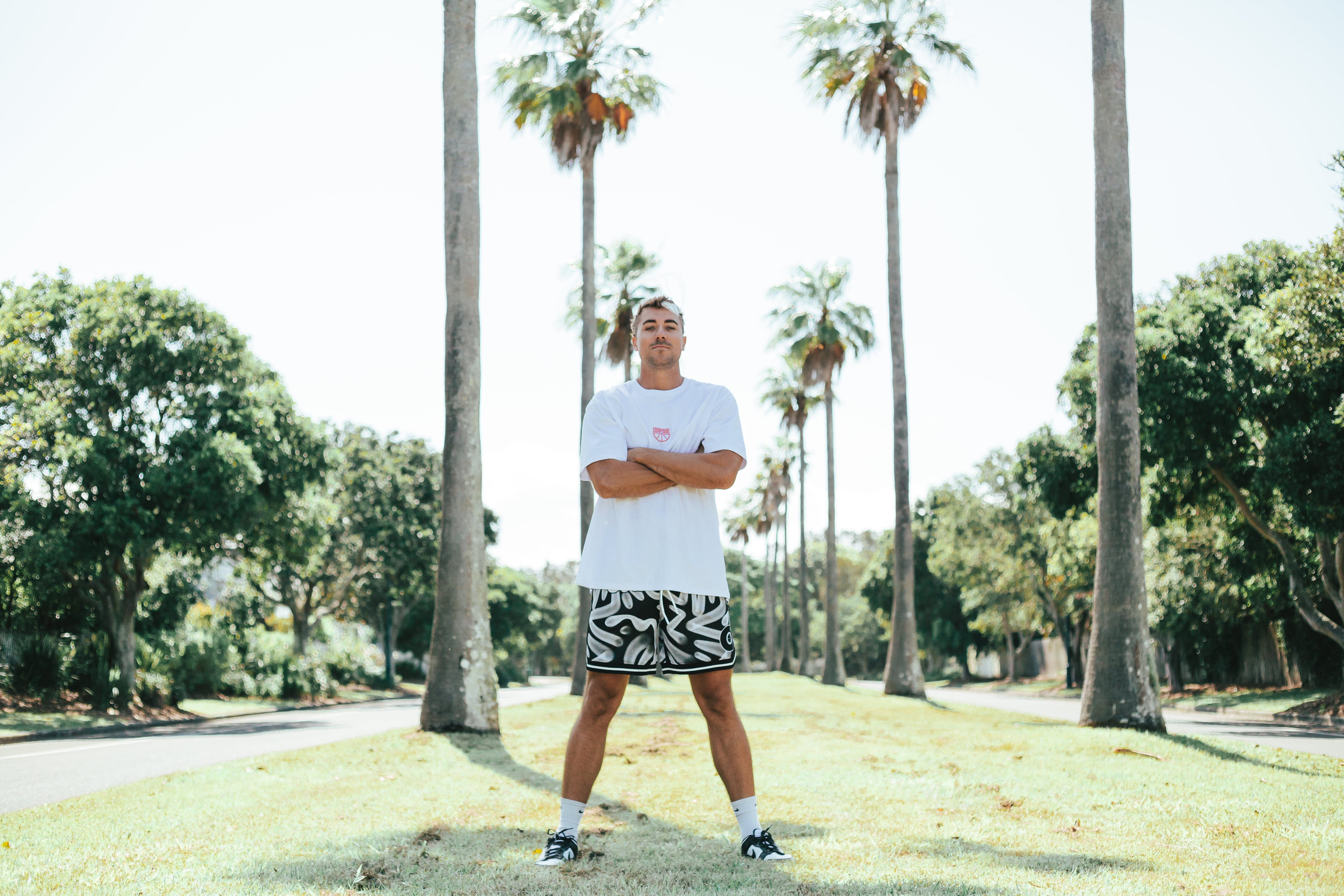 Courtside ROTY basketball shorts shown on Nelson NBL player with white hooper tee with red print, standing cross armed with palm trees