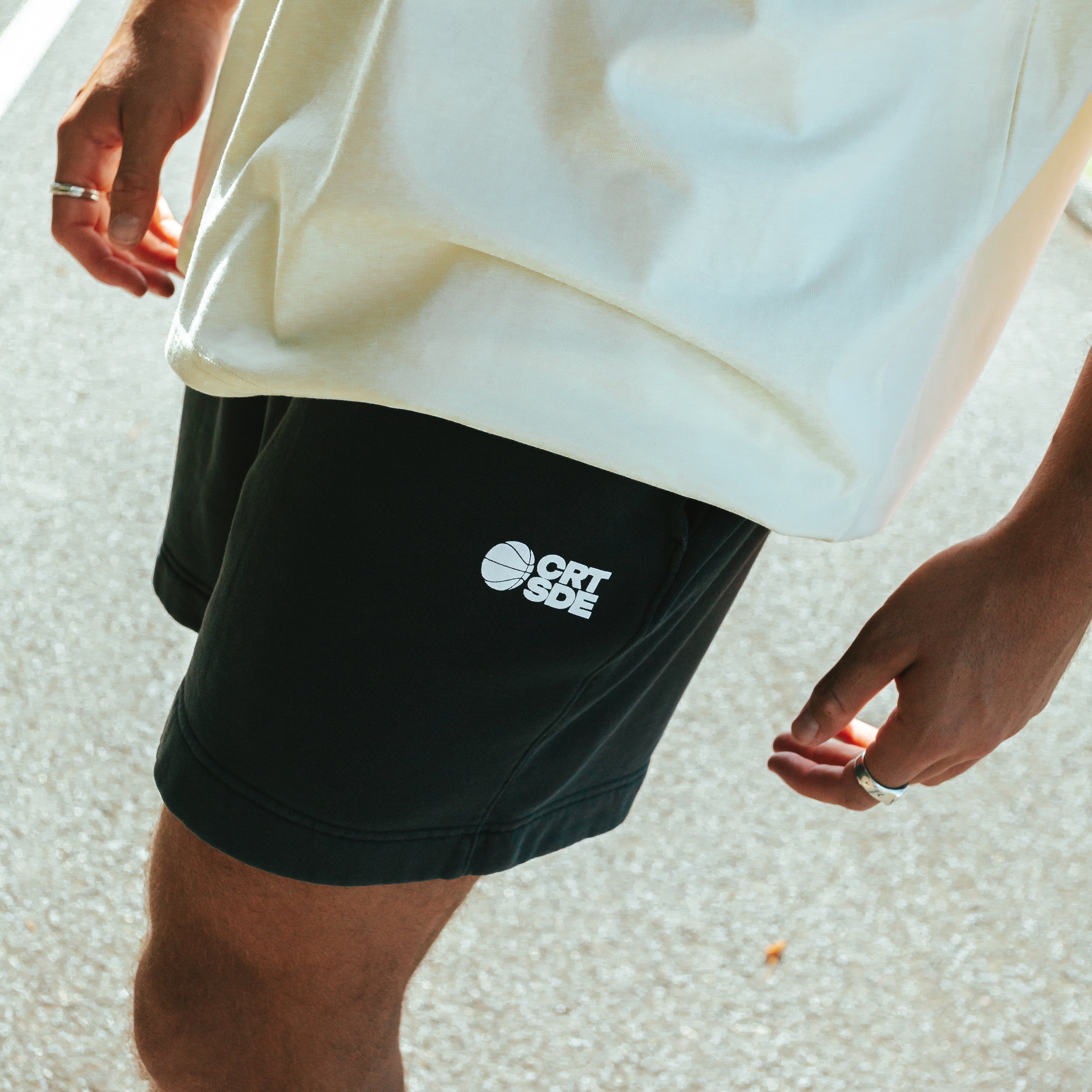 A person wearing a butter yellow t-shirt and black faded shorts with the brand logo 'Courtside' visible on the shorts.