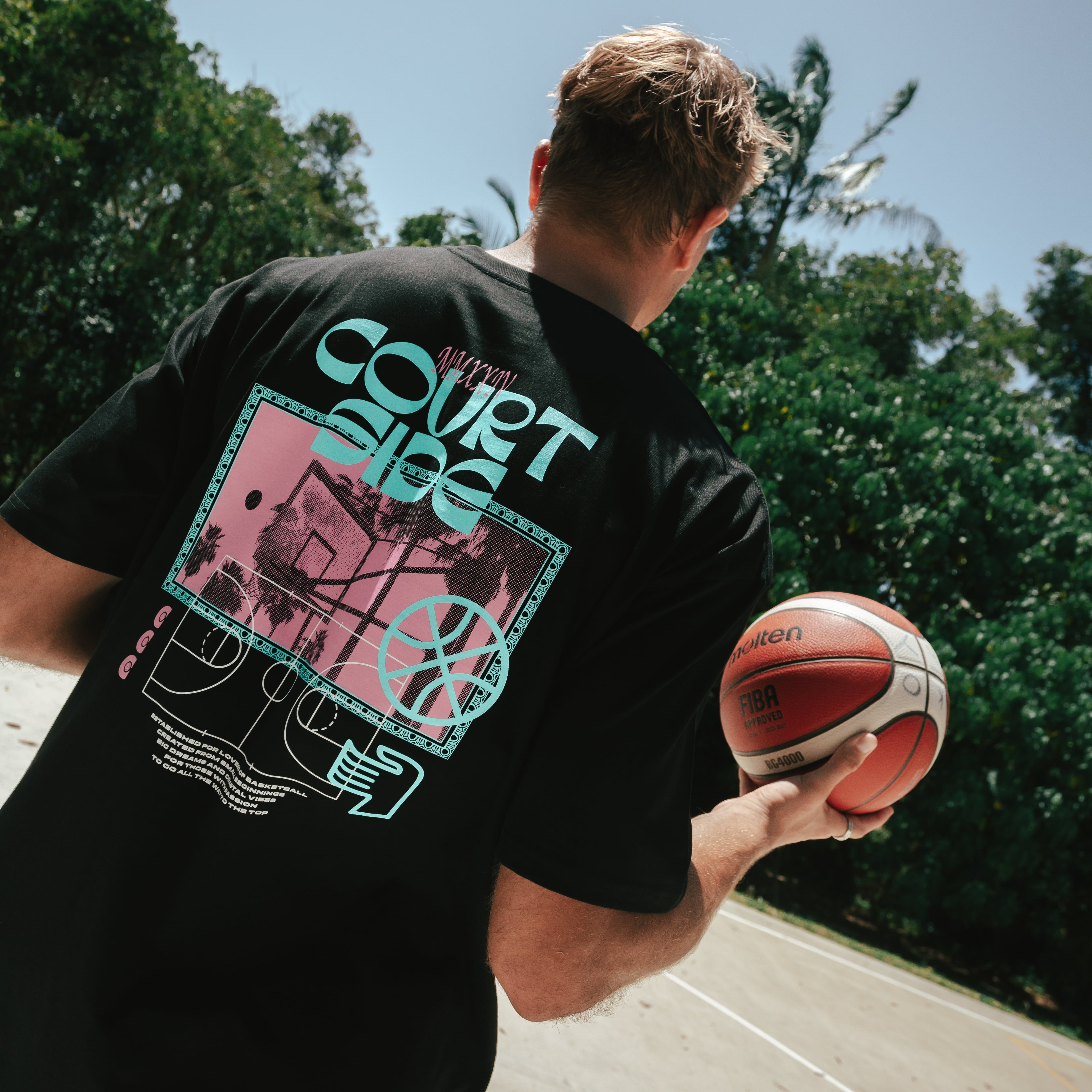 A person wearing a black Vibes Tee with a basketball and text graphic on it, standing outdoors.