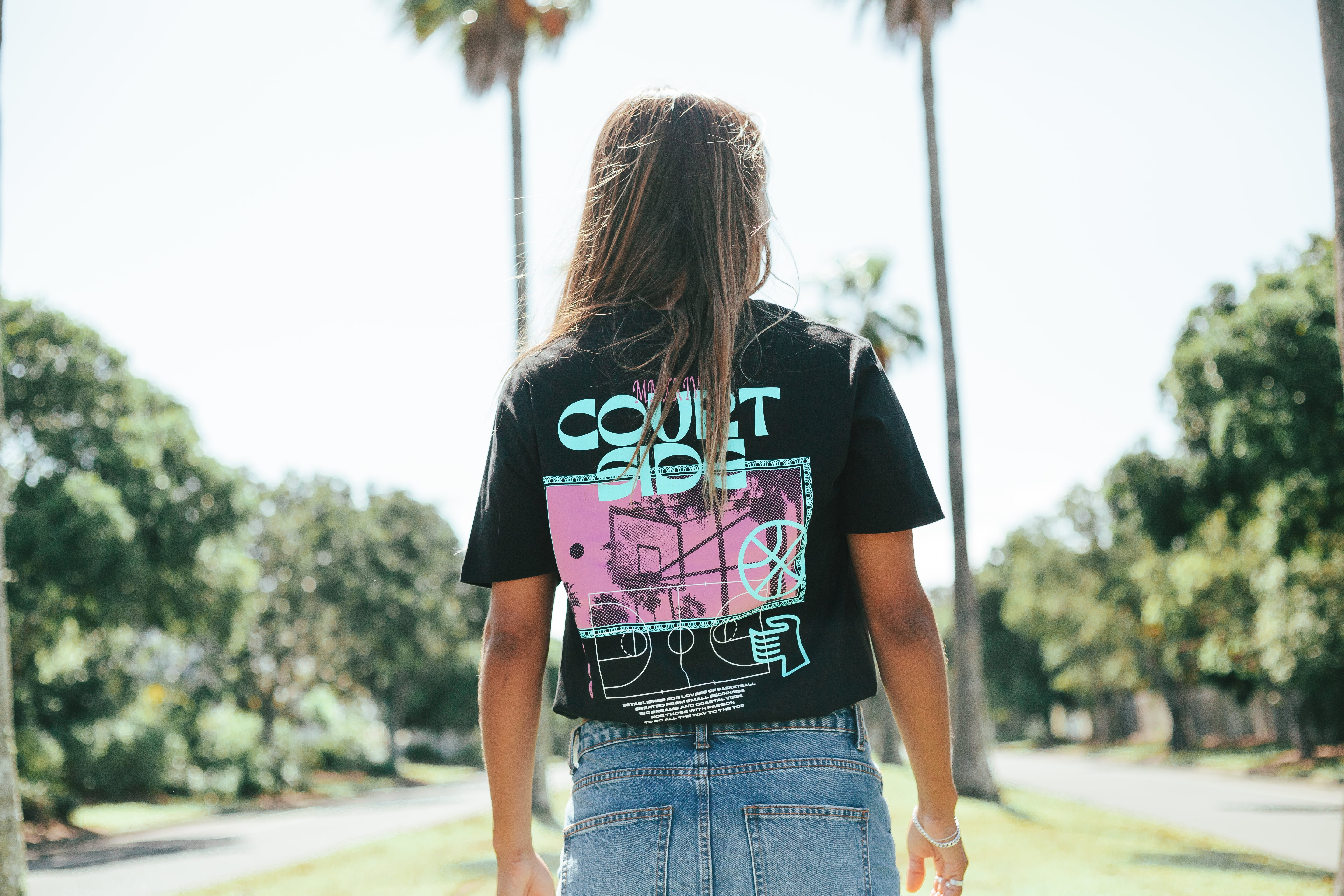 Courtside Vibes Tee in black - back view lifestyle worn by female with palm trees in background