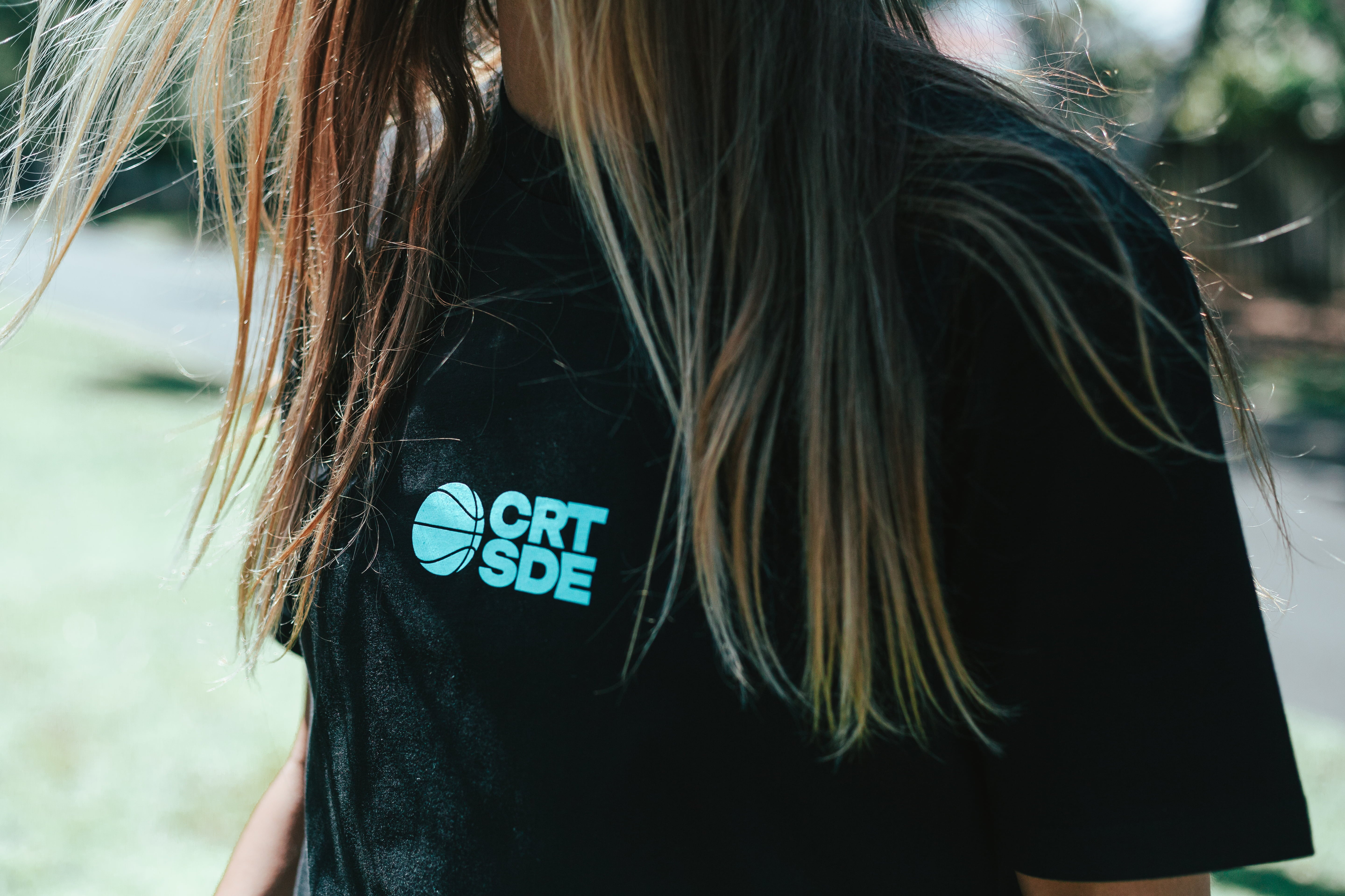 female wearing black vibes tee with long hair, showing teal logo detail on front
