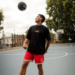 Person playing basketball on an outdoor court with trees and buildings in the background