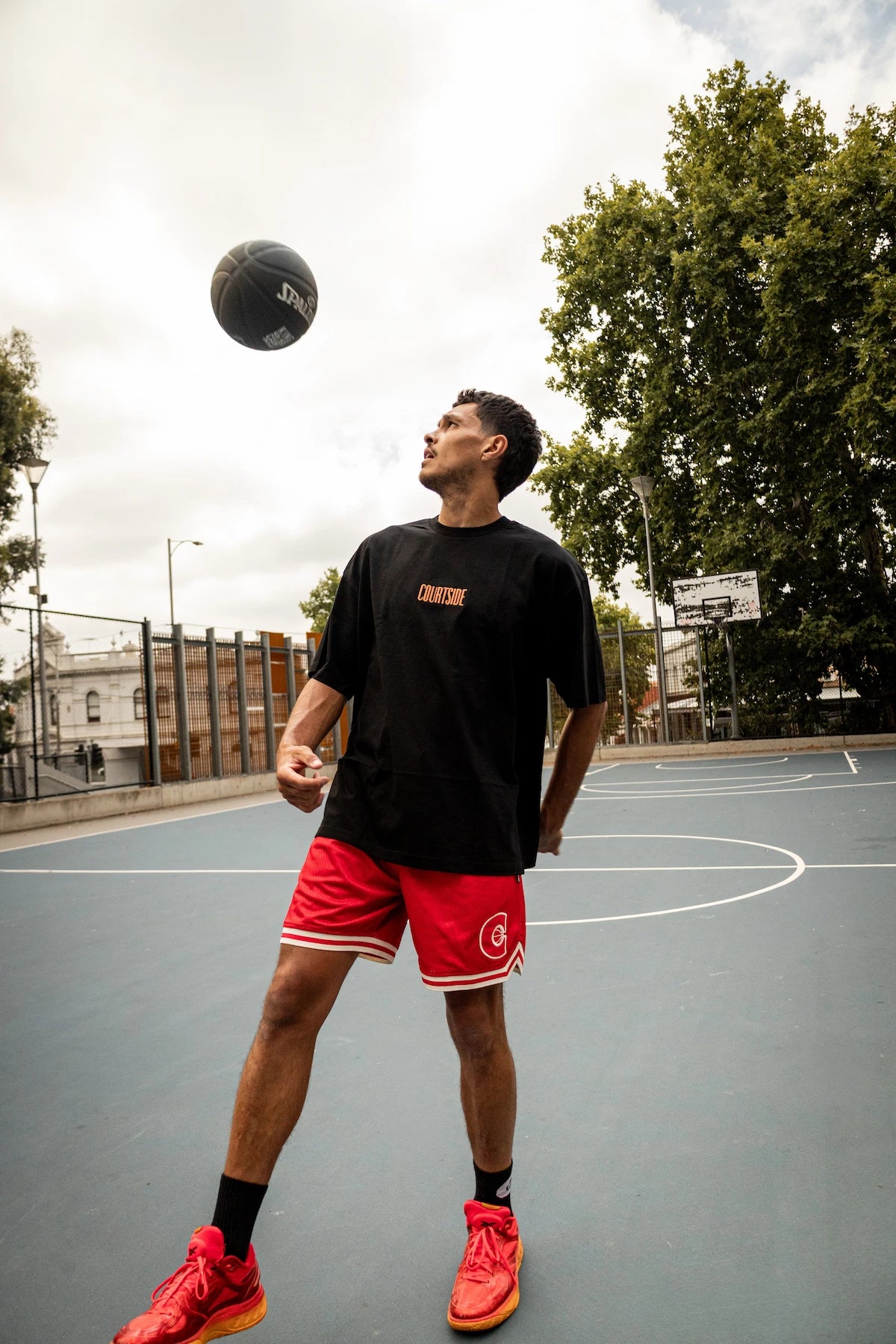 Person playing basketball on an outdoor court with trees and buildings in the background