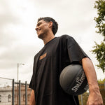 Man holding a basketball on an outdoor court with a cloudy sky in melbourne
