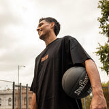 Man holding a basketball on an outdoor court with a cloudy sky in melbourne