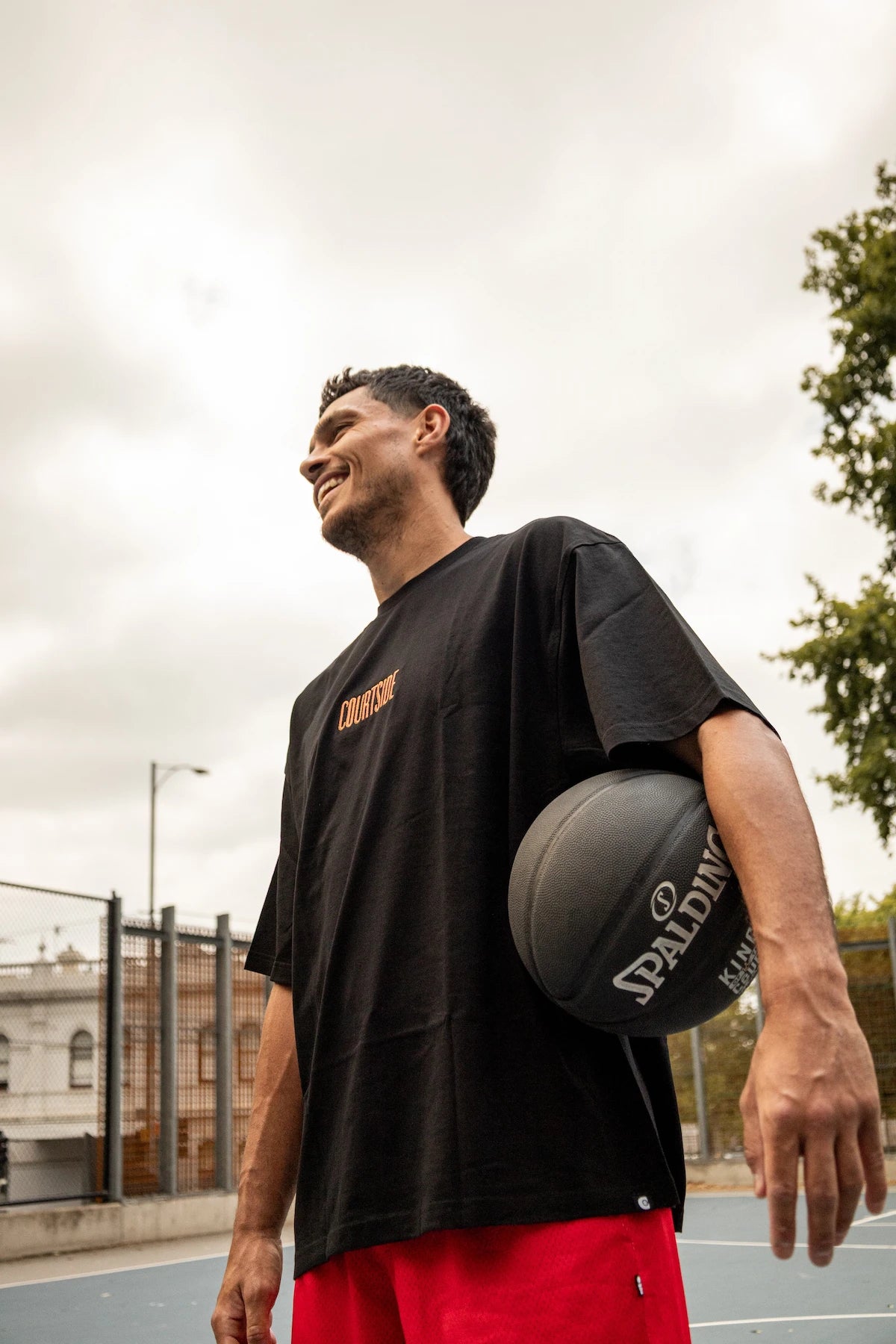 Man holding a basketball on an outdoor court with a cloudy sky in melbourne